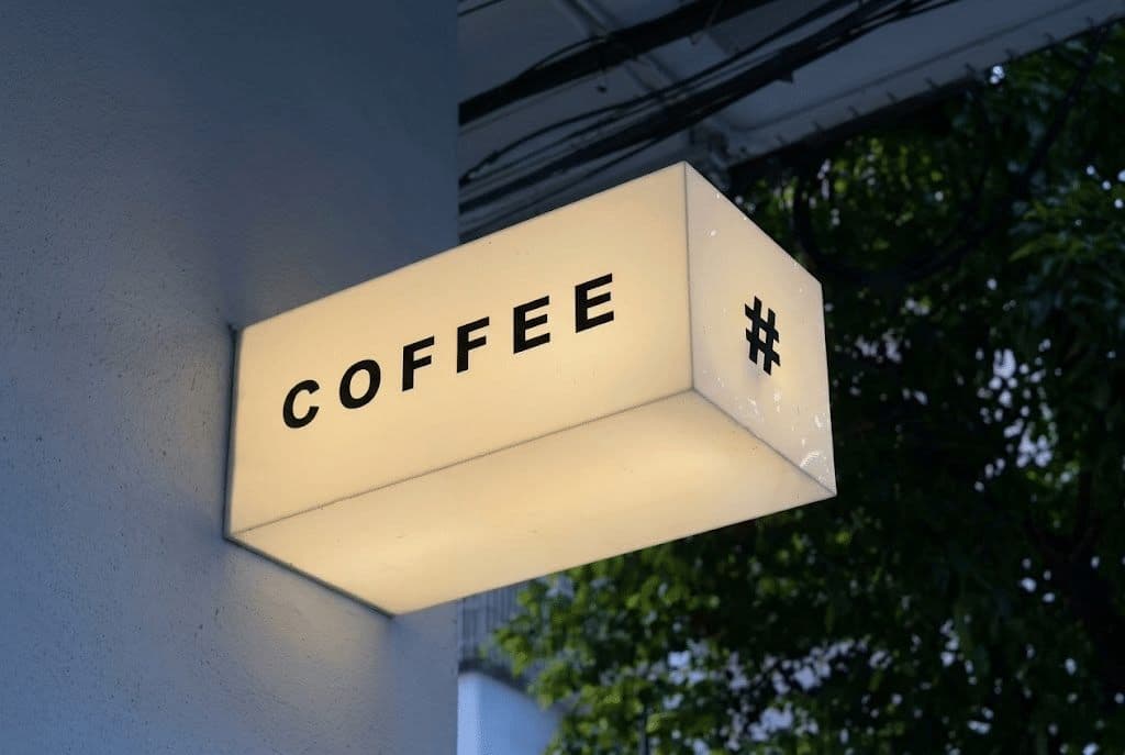 Leuchtkasten COFFEE mit Schriftzug und warmem Licht an der Außenwand.