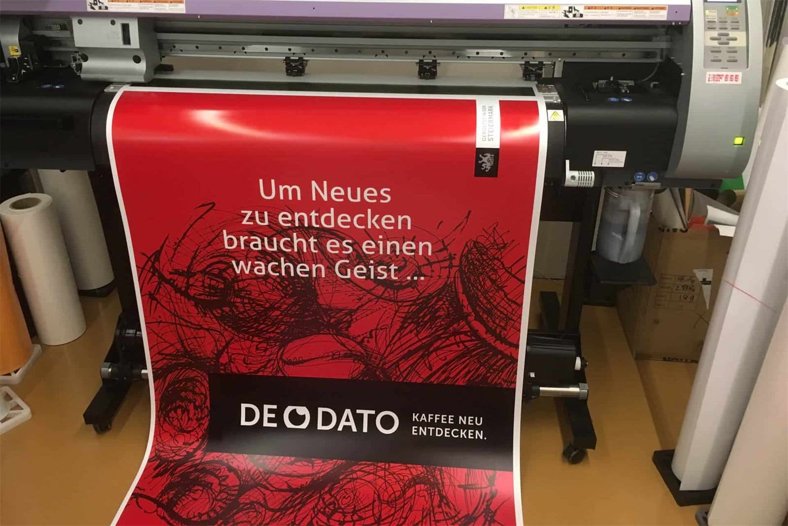 Roll-up-Banner für De Dato Kaffee wird auf einem Großformatdrucker ausgedruckt – rotes Design mit Schriftzug und steirischem Panther